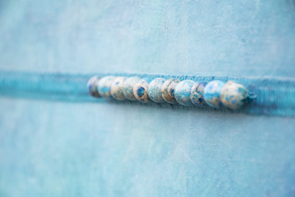 Detailed view of stone beads on Tranquility, a mixed media painting in shades of blue and green by artist Heather Elliott. 